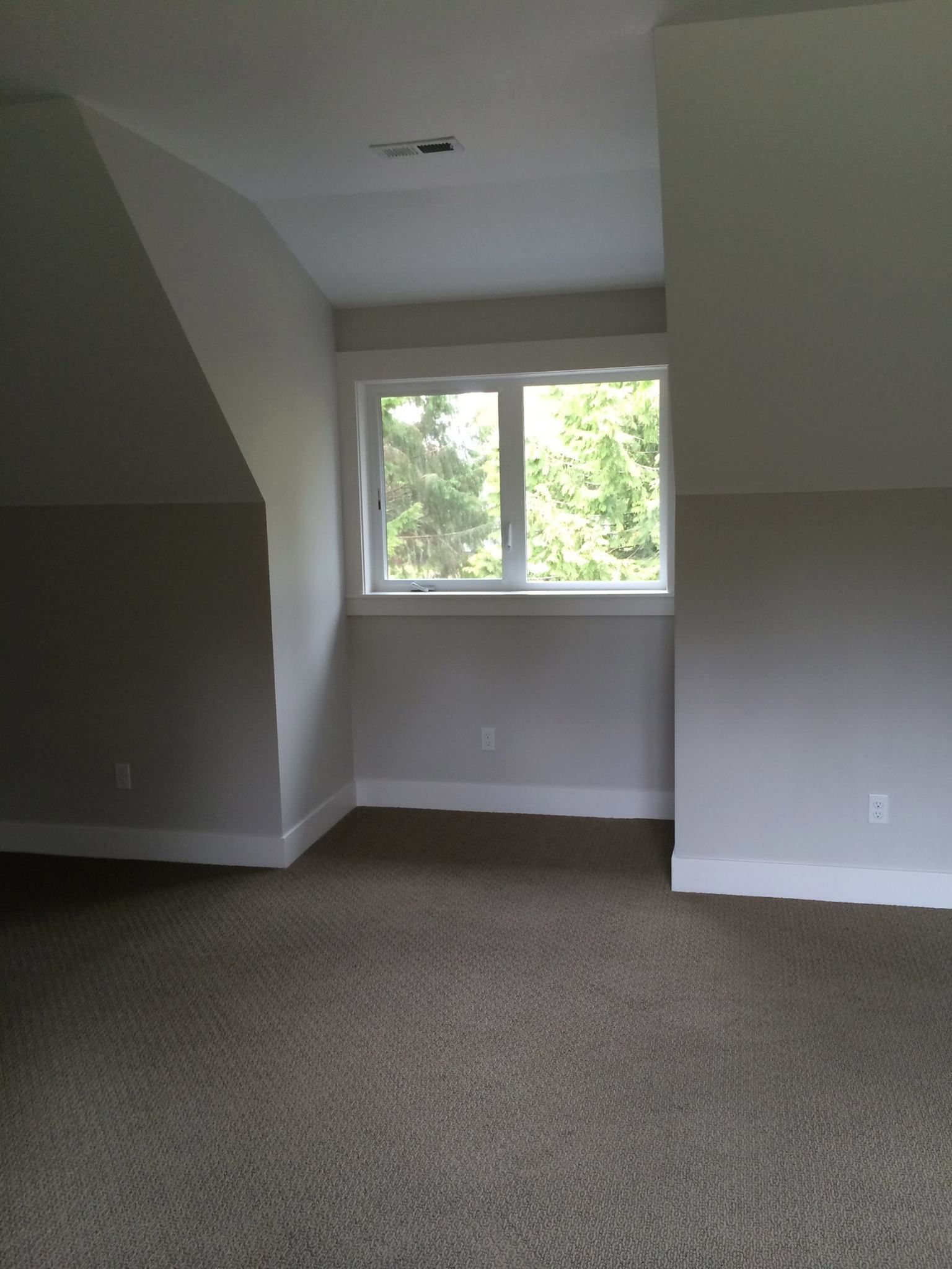 A room with a window, carpet, and sloped walls, painted gray and white.