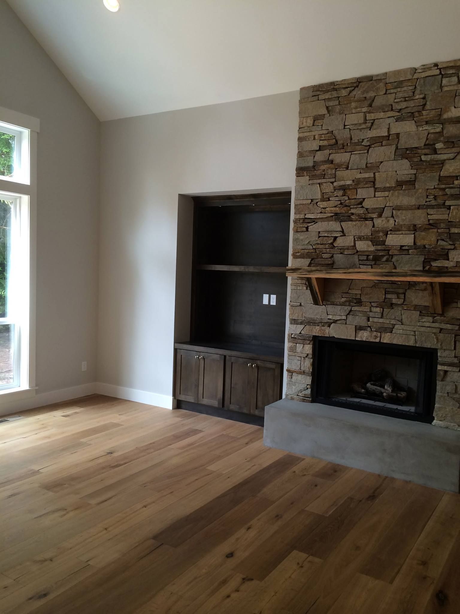 Living room with stone fireplace, built-in shelves, hardwood floor, and large window.