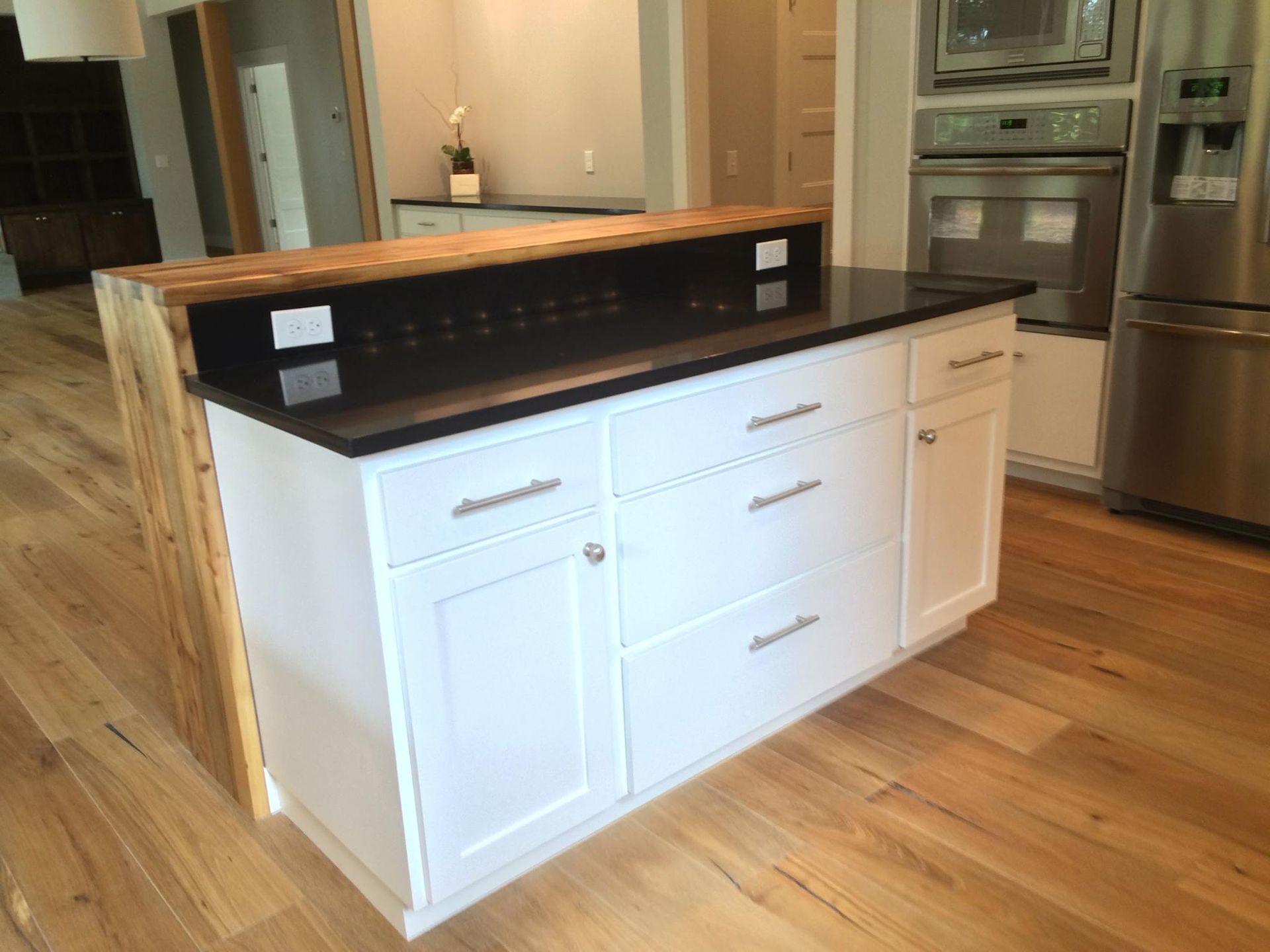 Kitchen island with white cabinets, black countertop, and wooden bar top.