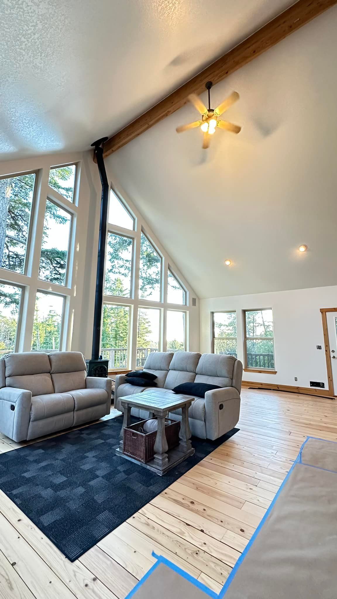 Spacious living room with large windows, fireplace, light-colored couches, and a dark blue rug.