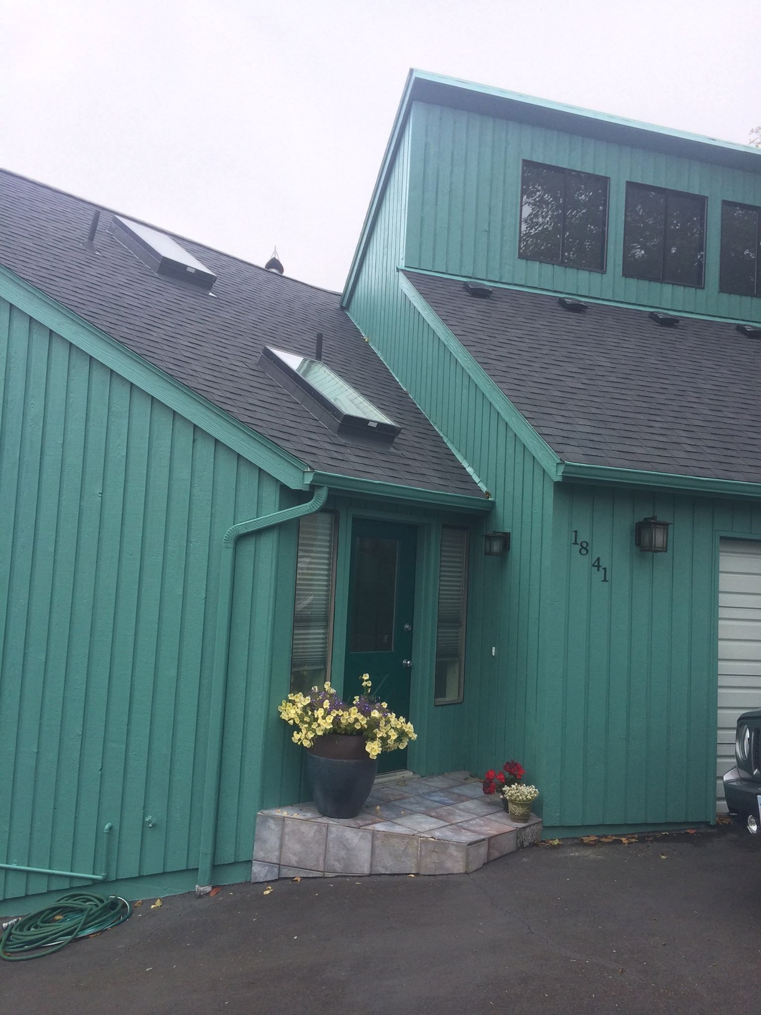 Green-painted house with dark roof and stone entrance. Flowers decorate the doorway.