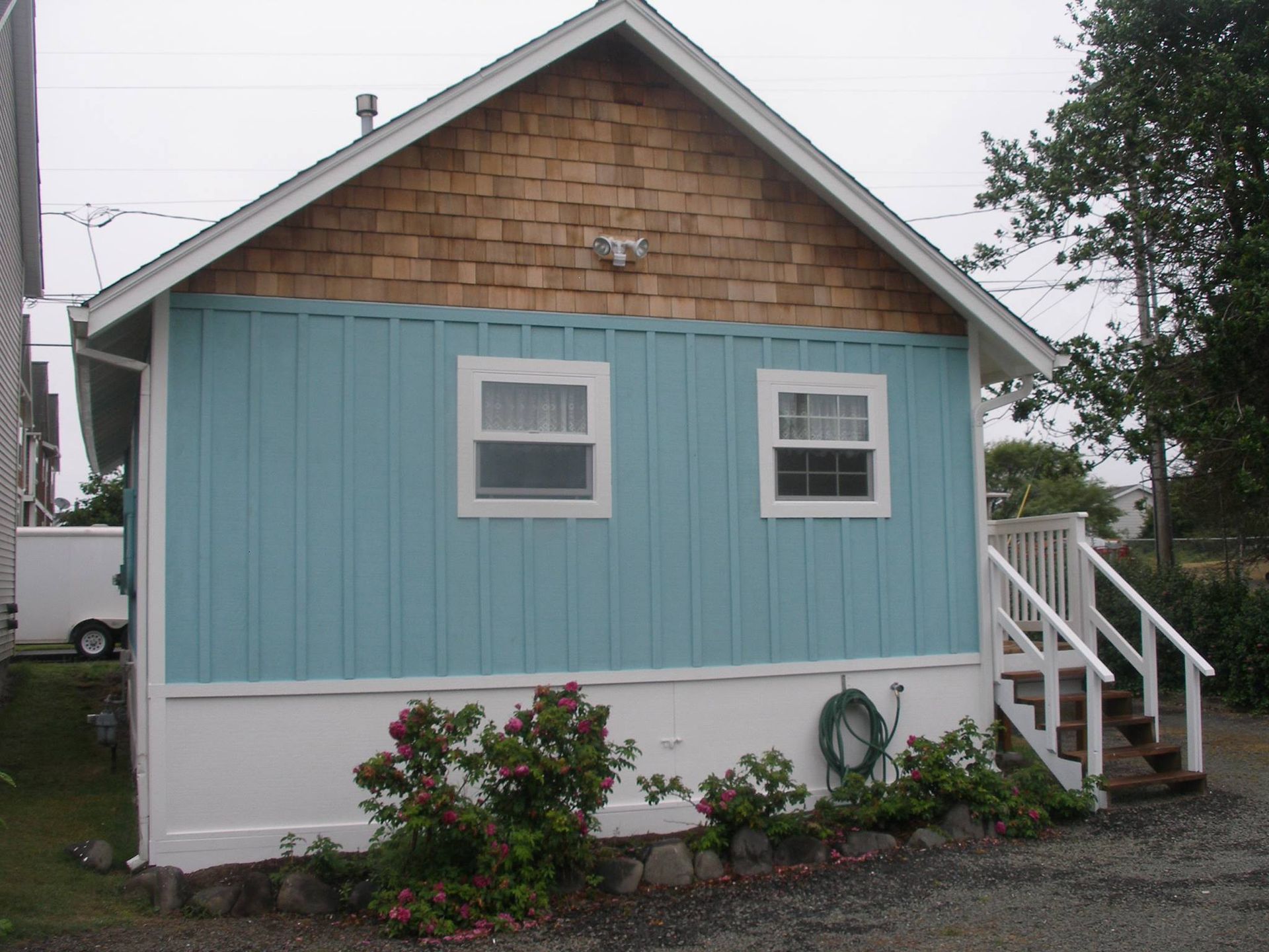 Blue and white cottage with cedar shake gable, two windows, and small stairs.