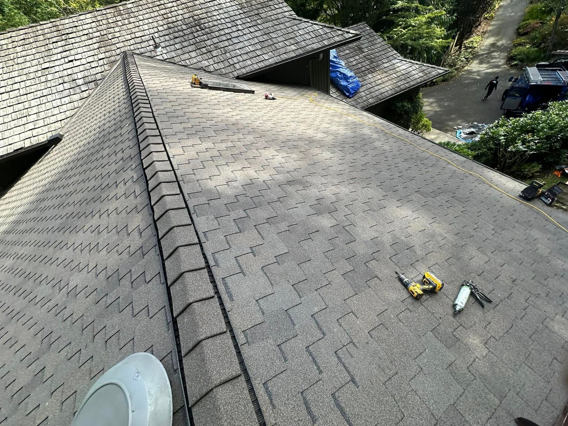 A grey shingle roof with tools and a vent, viewed from above.