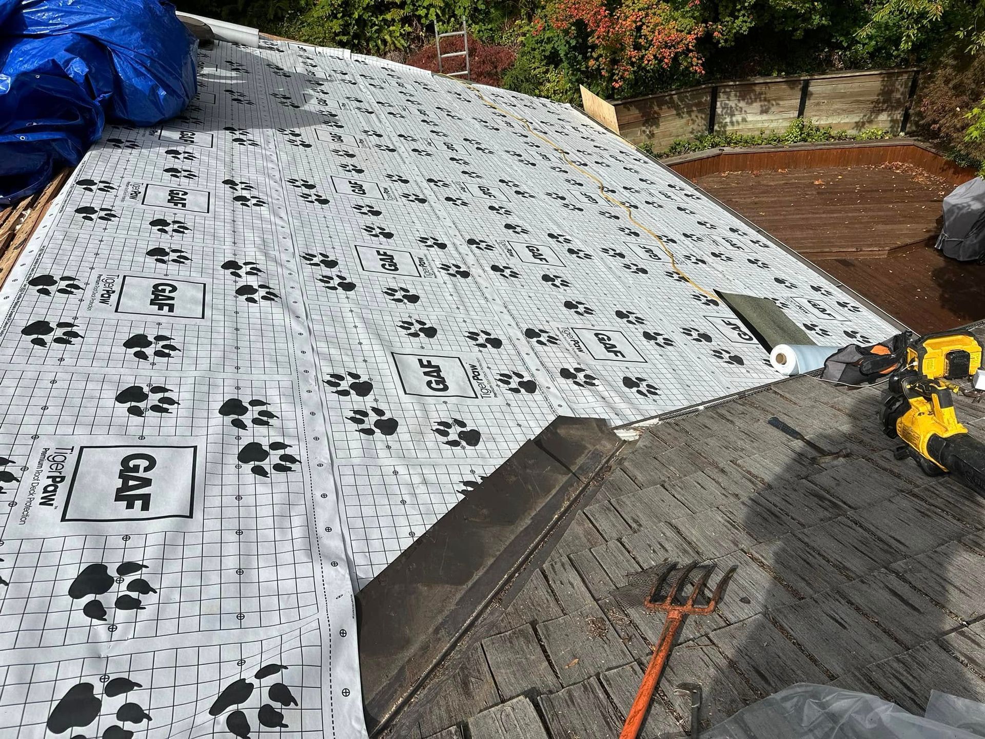 Roofer installing underlayment with paw print pattern; tools and tarp on a sloped roof.