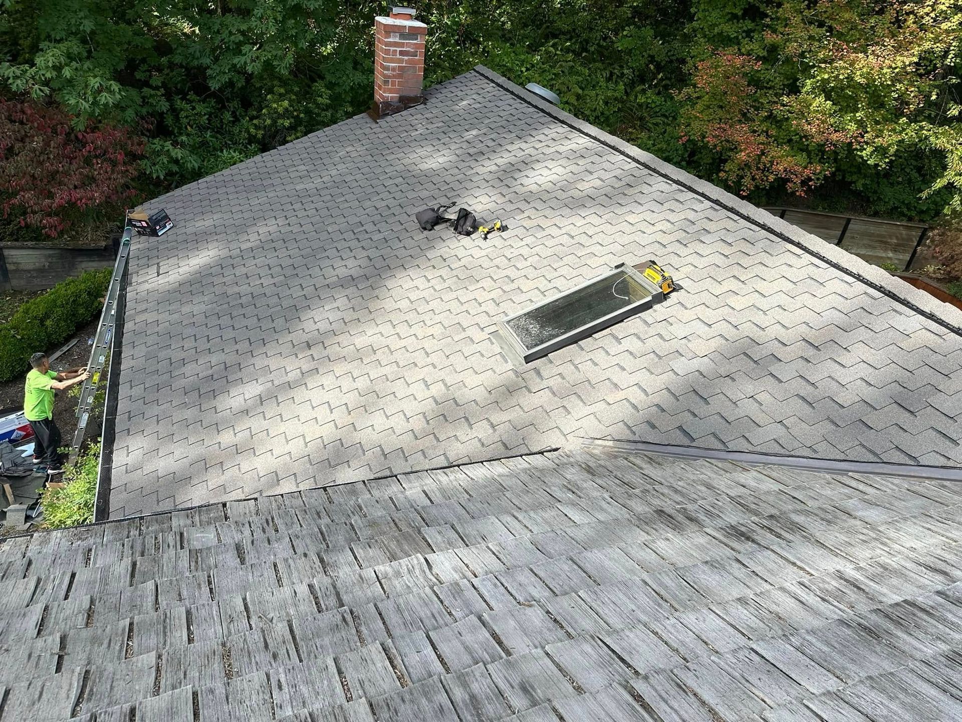 Rooftop with construction tools and skylight; person in green shirt is working on the edge of the roof.