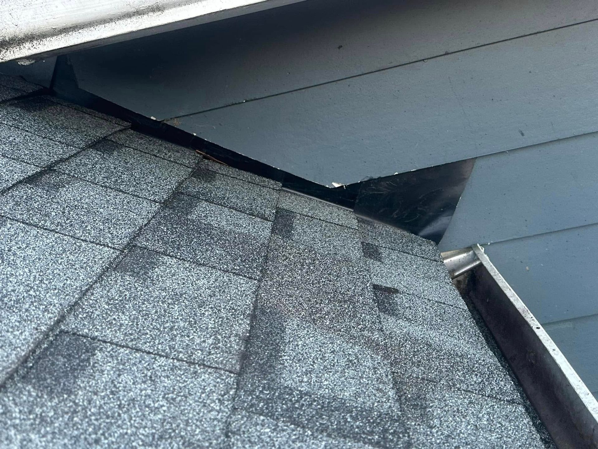 Roof shingles meeting siding and gutter. Overhang with dark space between.