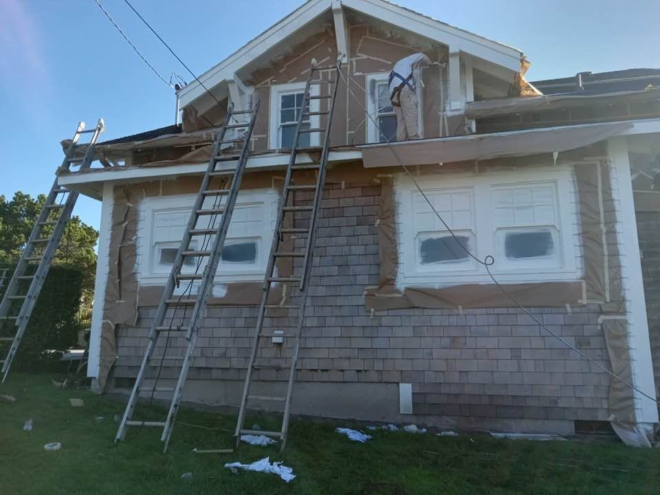 House with ladders, undergoing renovations; person working on the upper window; blue sky.