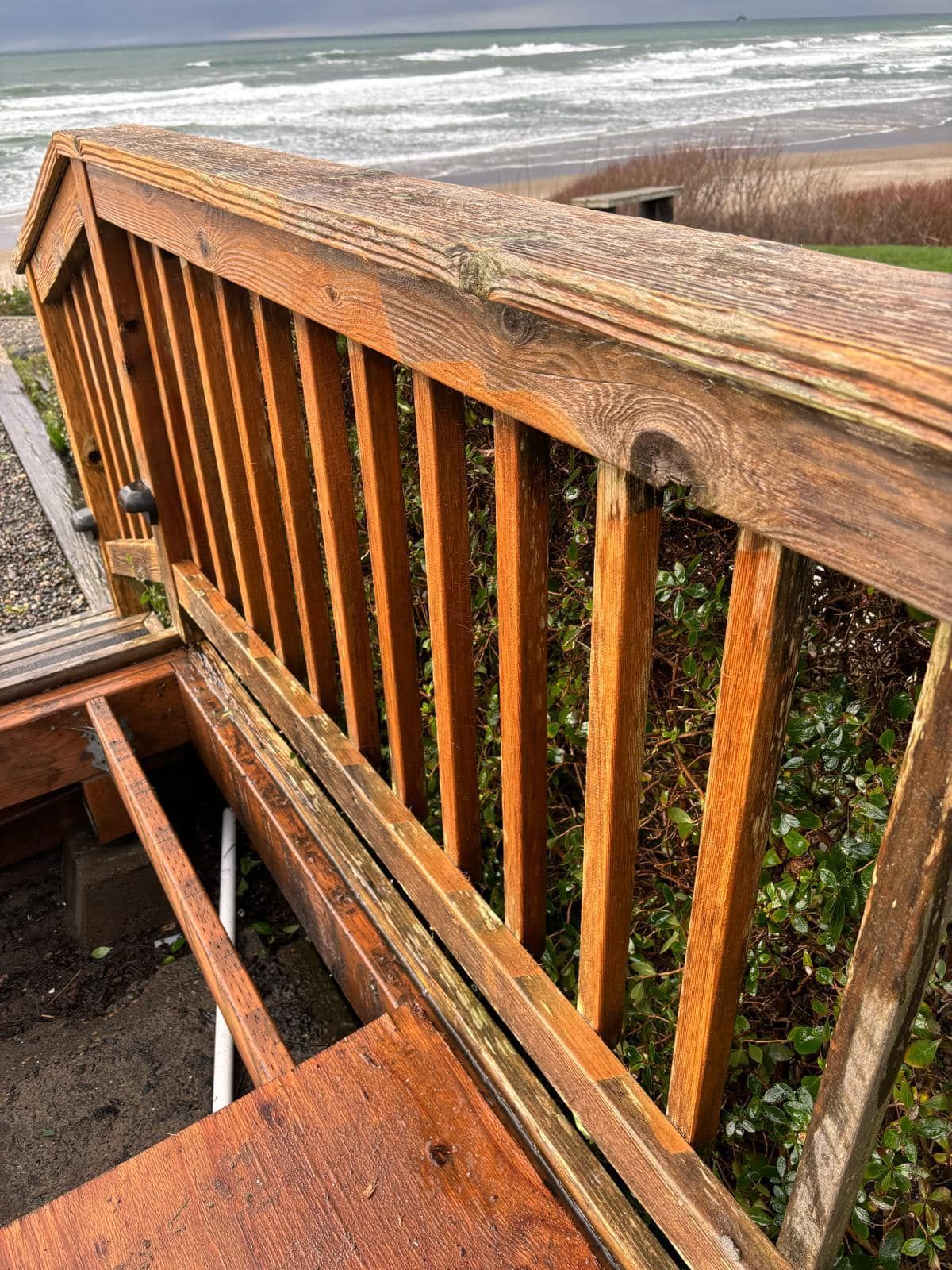 Wooden deck railing overlooking the ocean with a cloudy sky.