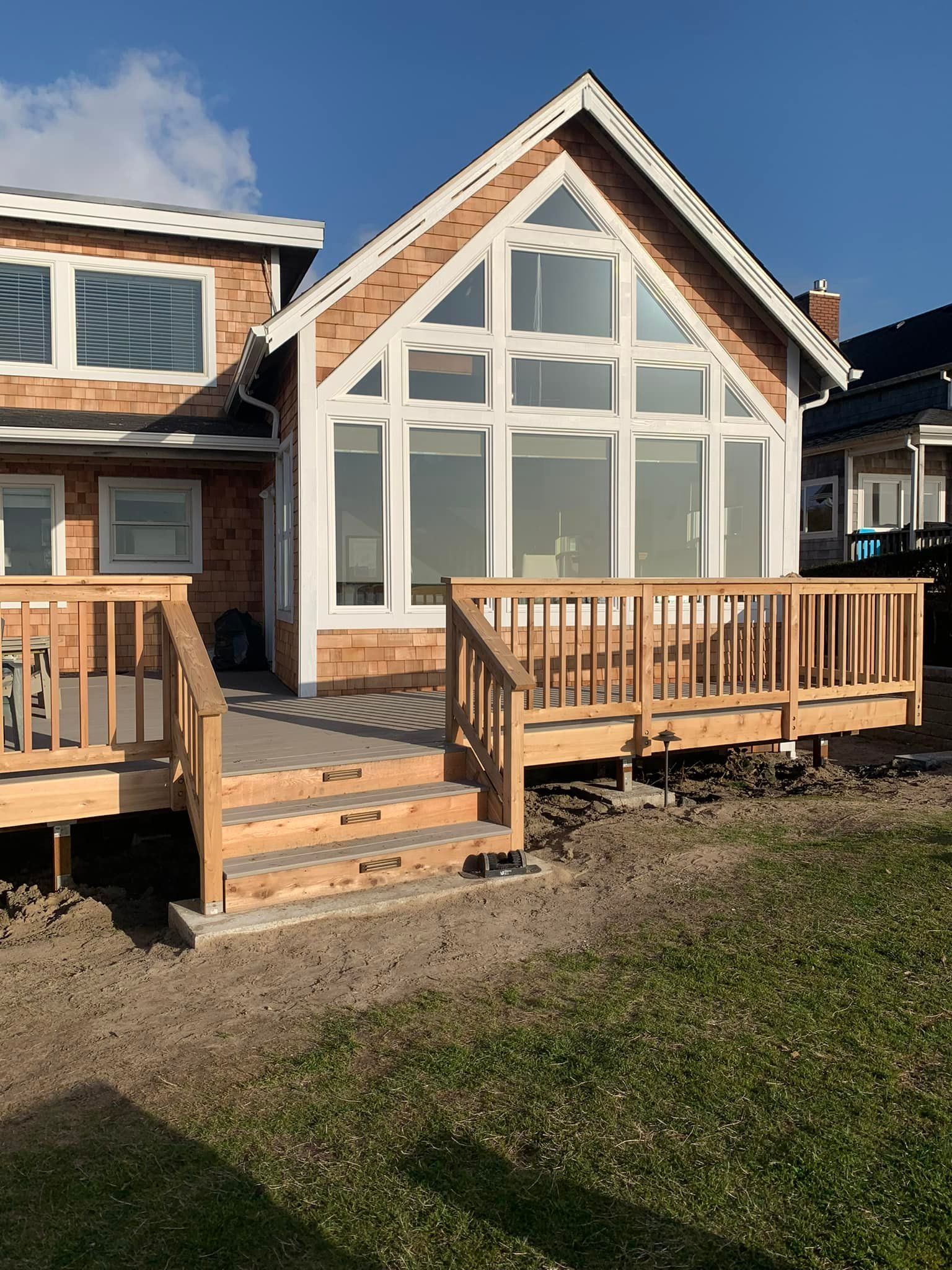 Wooden deck and steps leading to a house with large windows, blue sky.
