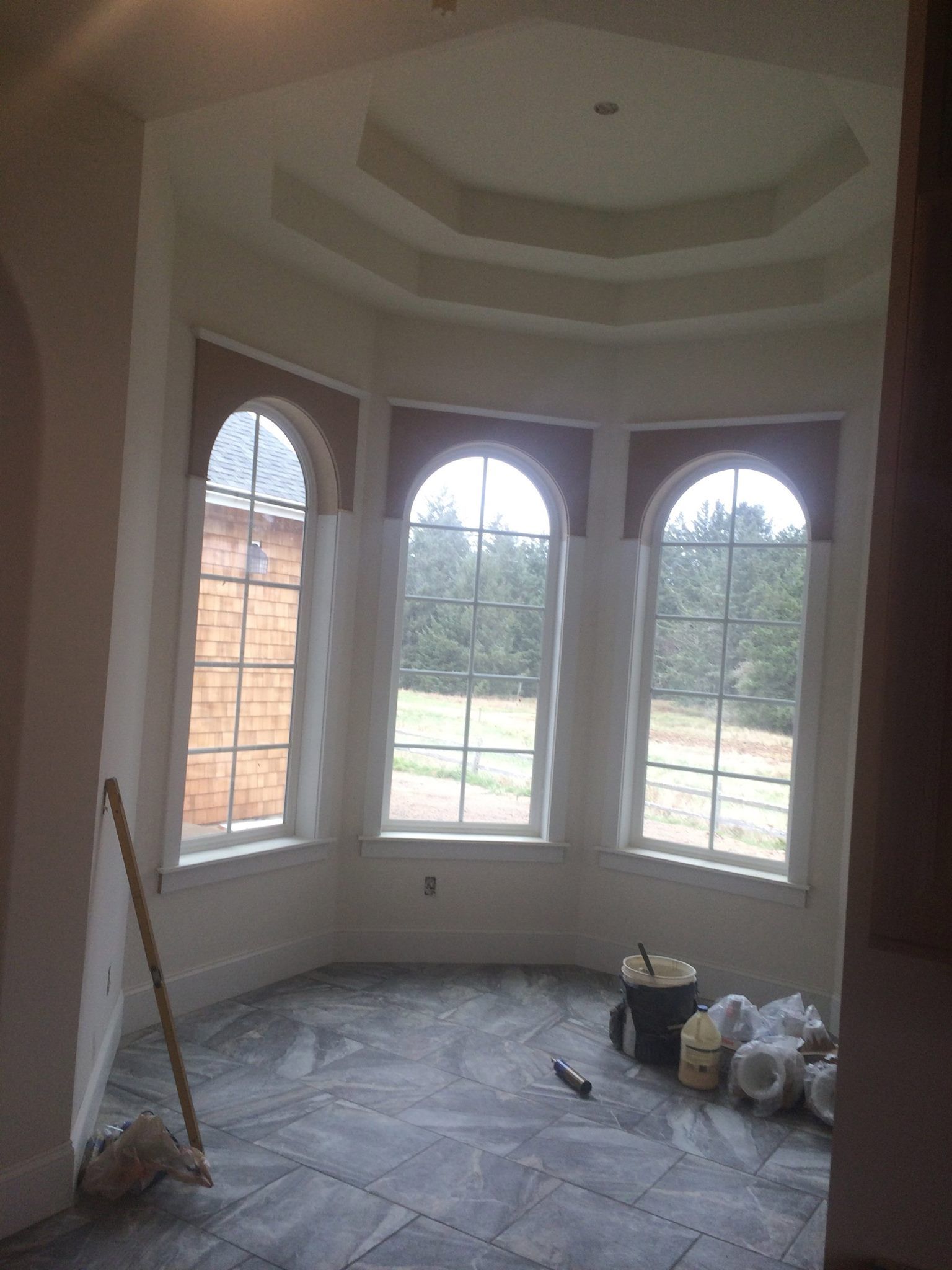 Interior of room with curved windows, brown trim, and unfinished floor; bucket and supplies present.