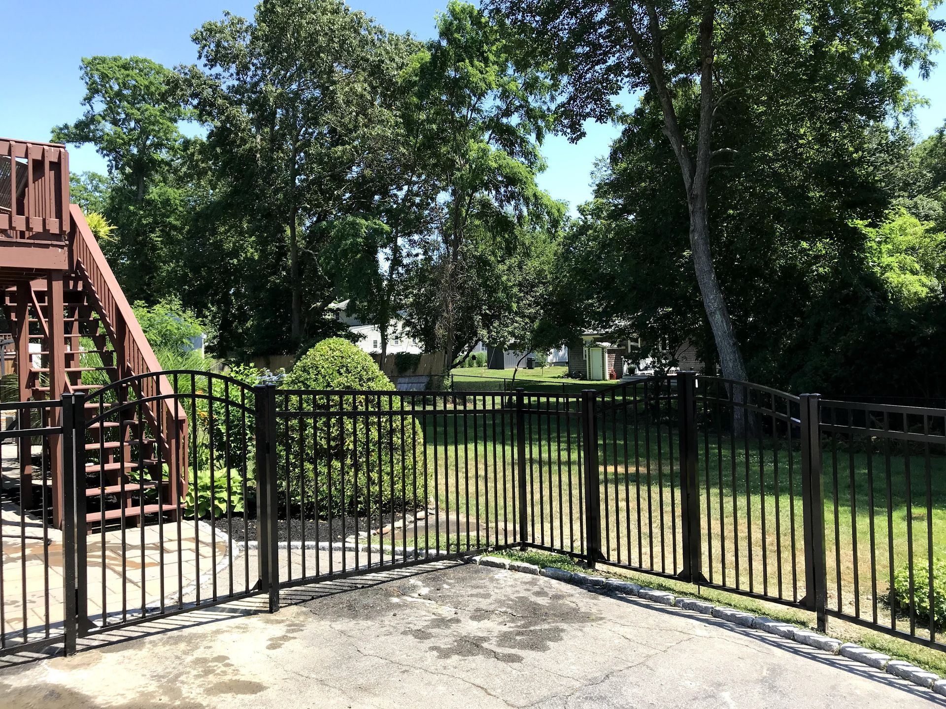 A metal fence surrounds a lush green yard with a wooden deck in the background.