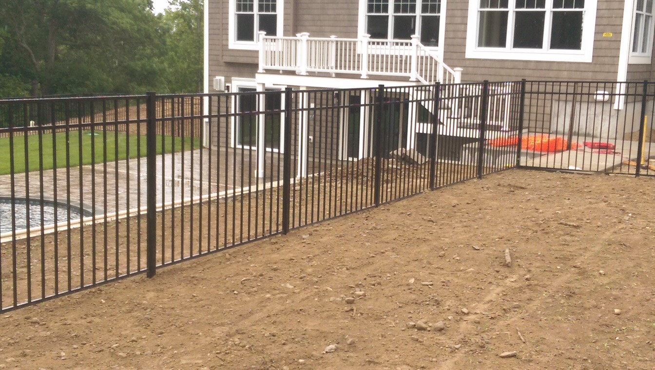 A metal fence surrounds a dirt field in front of a house.