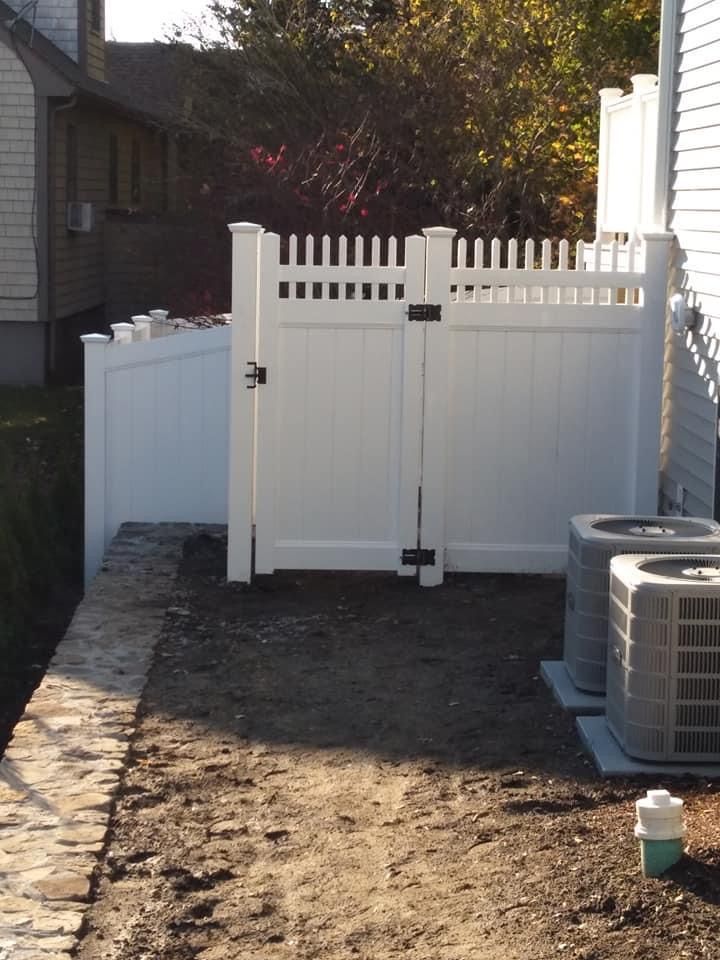 A white fence with a gate and two air conditioners in front of it
