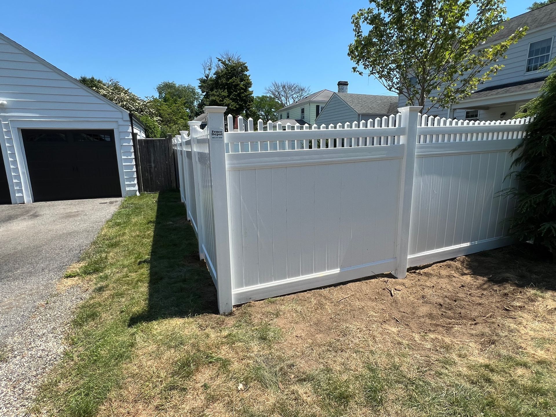 A white fence surrounds a yard next to a garage.