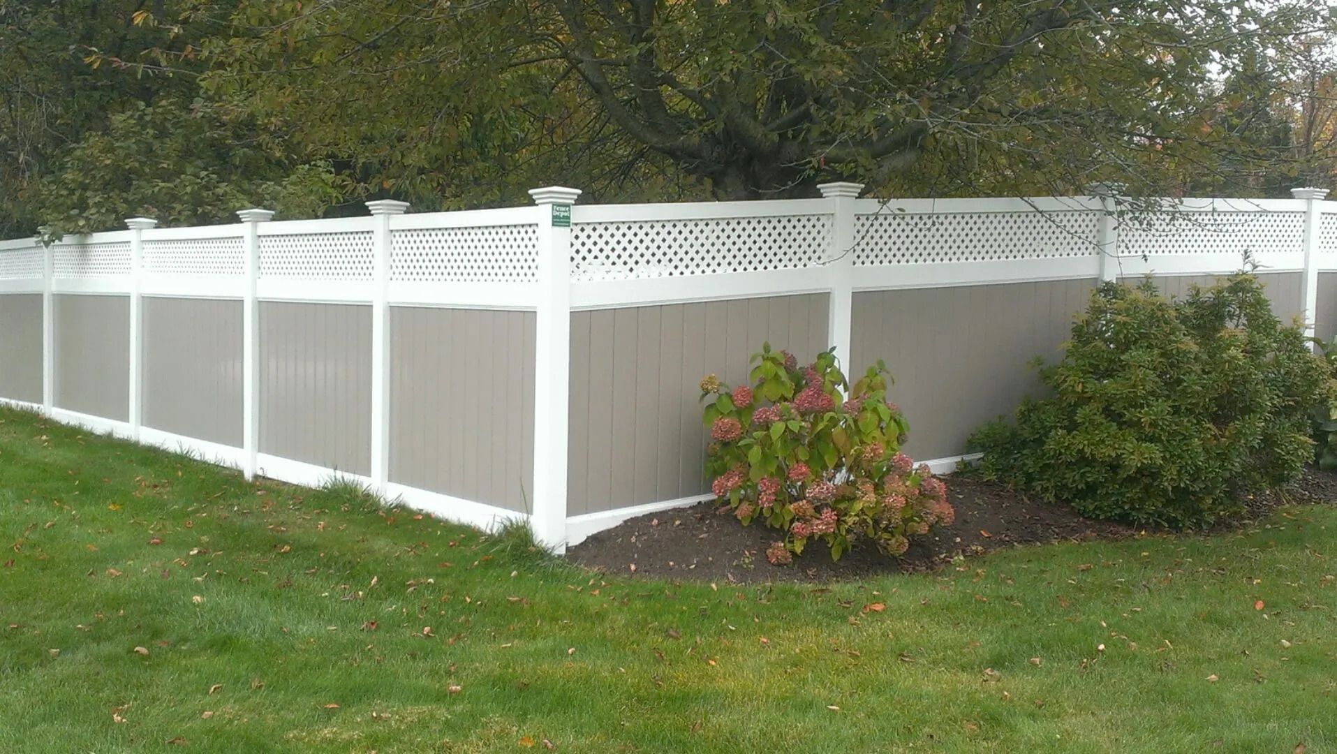 A white and tan fence is sitting in the middle of a lush green field.