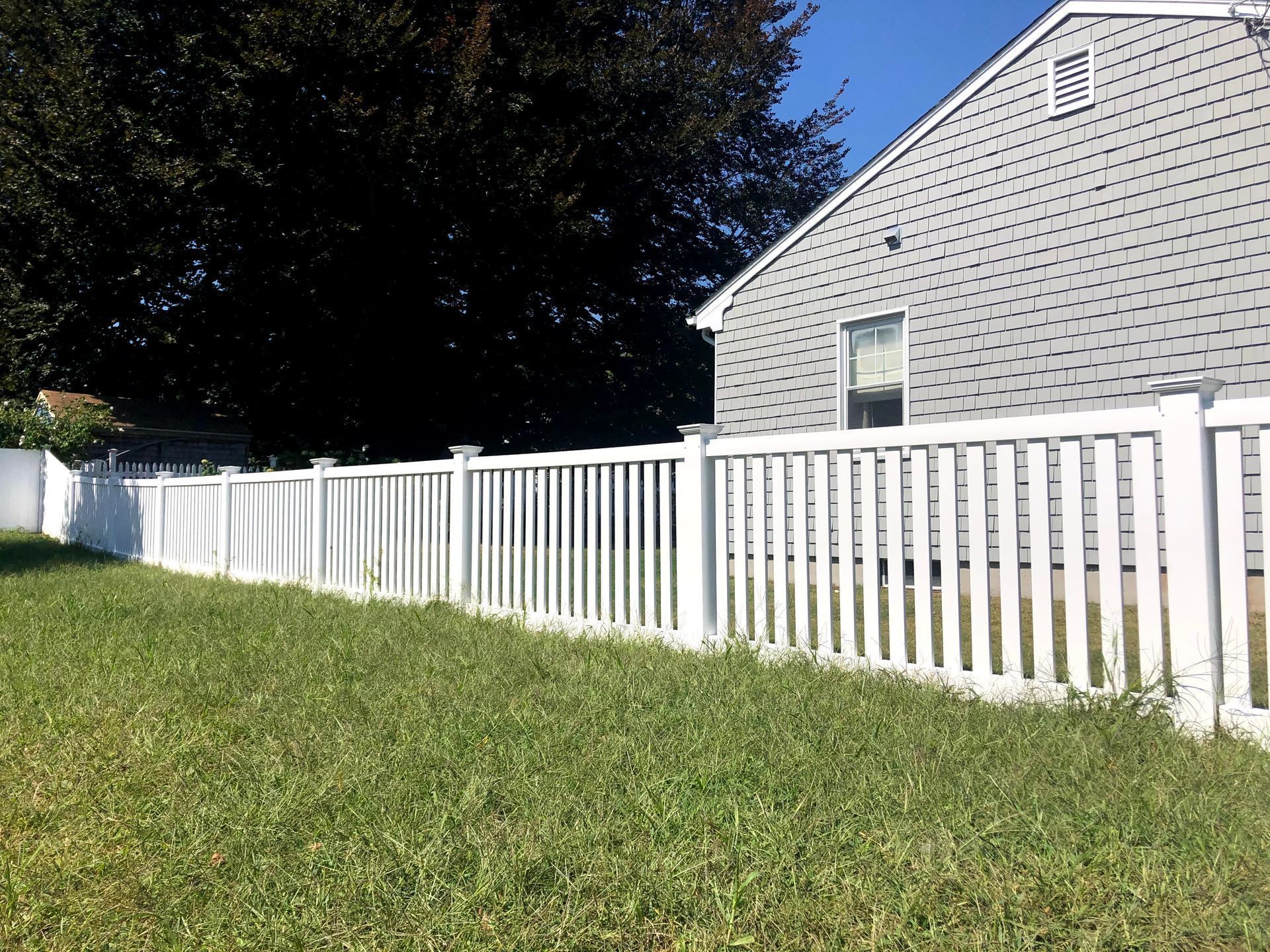 A white fence surrounds a lush green yard in front of a house.