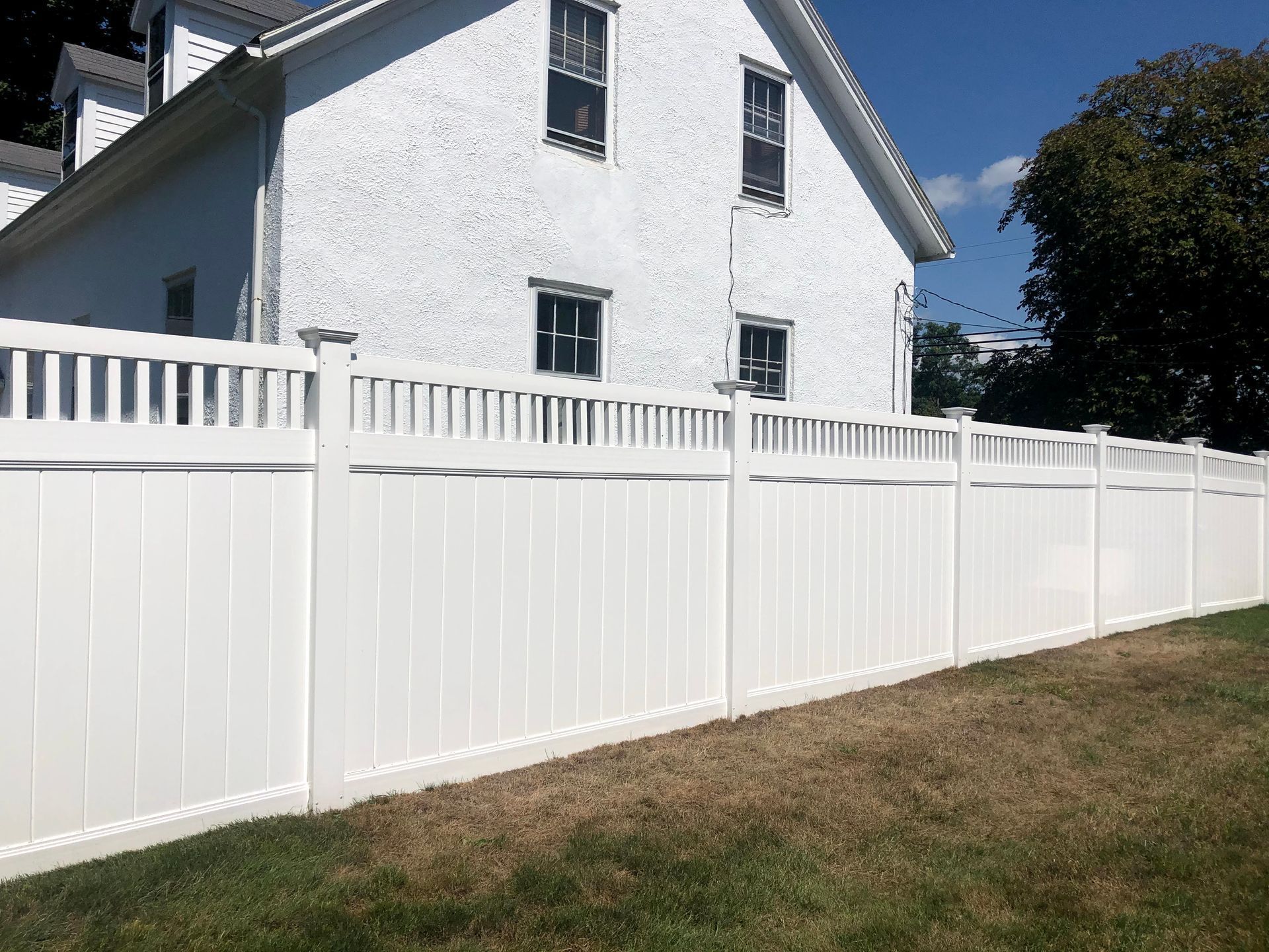 A white fence is in front of a white house.