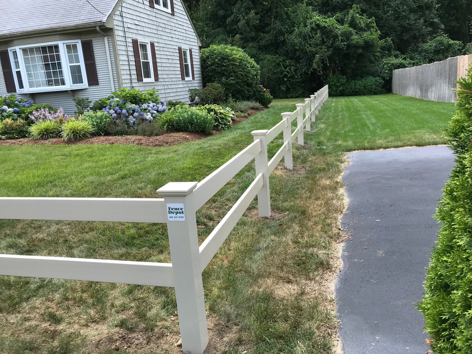 A white fence surrounds a lush green yard in front of a house.