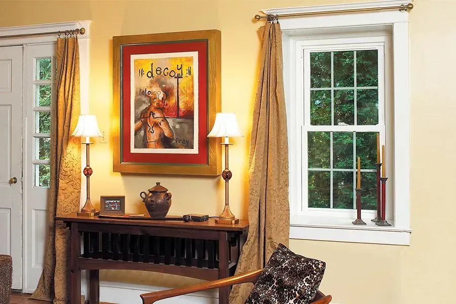 Living room with a painting, table, lamps, window, and chair. Warm colors, natural light.