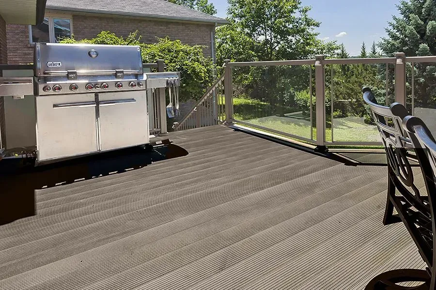 Composite deck with grill and glass railing, overlooking a yard.