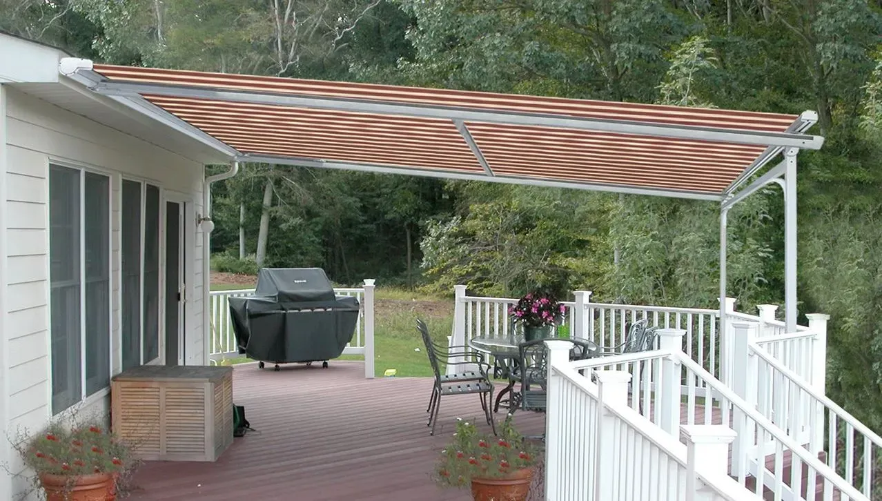 A retractable awning over a wooden deck with a grill, table, and railing.