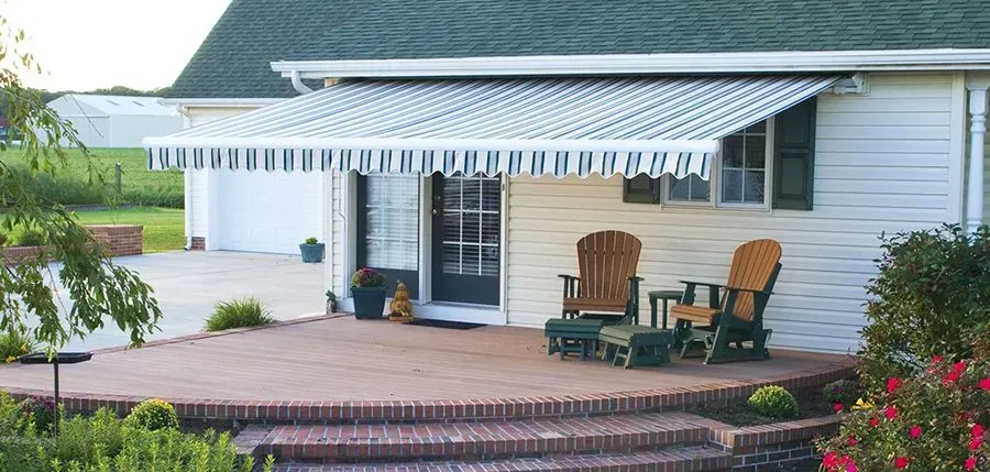 House exterior with striped awning, Adirondack chairs, and a brick patio.