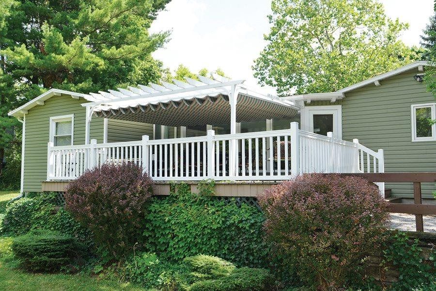 Green house with white deck, pergola, and shrubs.