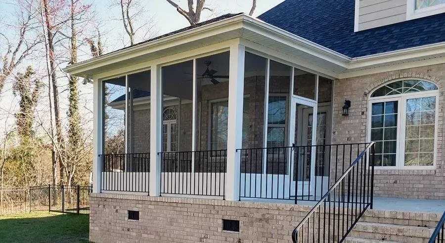 Screened-in porch attached to a brick house with black railings and steps.