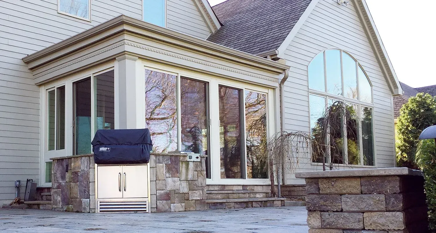 A residential backyard with a built-in grill, surrounded by windows and stone accents.