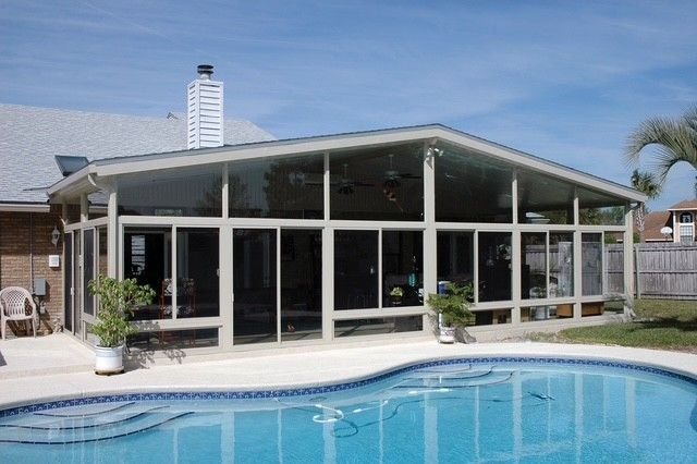 Sunroom addition with glass walls, attached to a brick house, overlooking a pool.