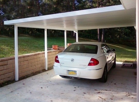 White car parked under a white carport with a brick retaining wall on the left.