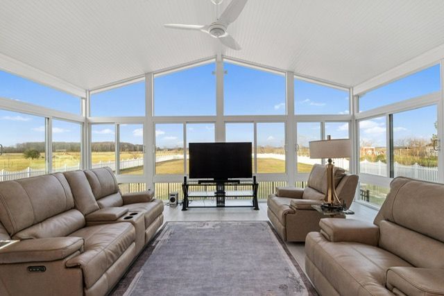 Sunroom with leather seating, large windows, TV, and area rug.