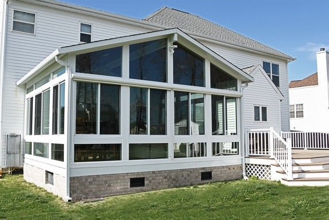 White sunroom addition with large windows attached to a white house, on a green lawn.