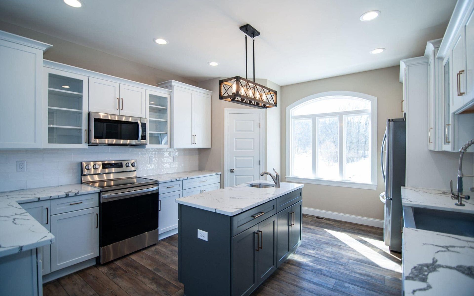 Bright modern kitchen with white cabinets, blue island, black appliances, and a window seat by arched windows
