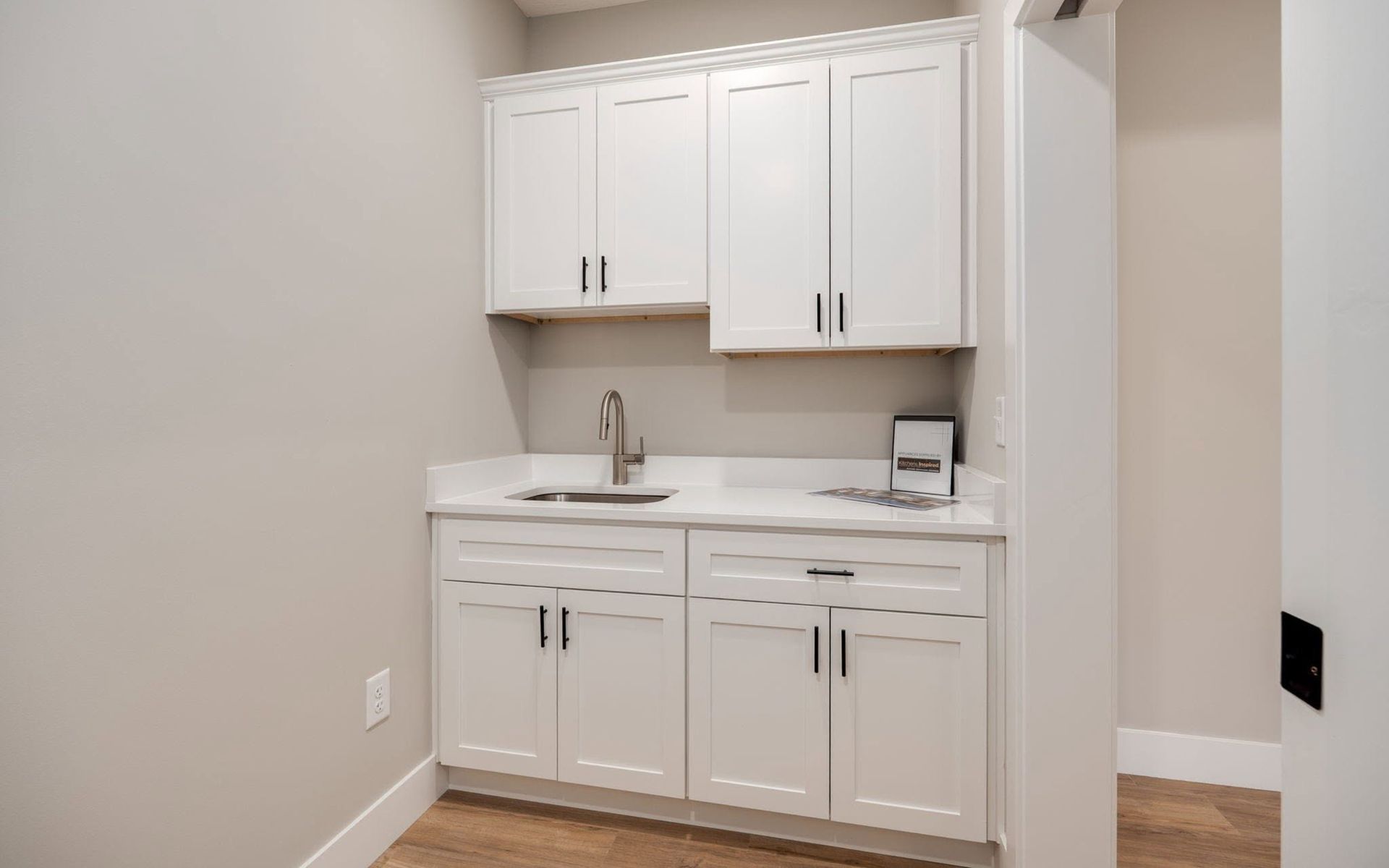 Small white kitchenette with cabinets, sink, and countertop against beige walls