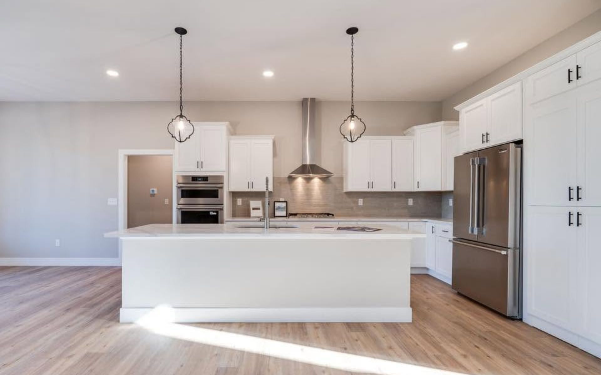 Modern white kitchen with island, stainless steel appliances, pendant lights, and hardwood floors