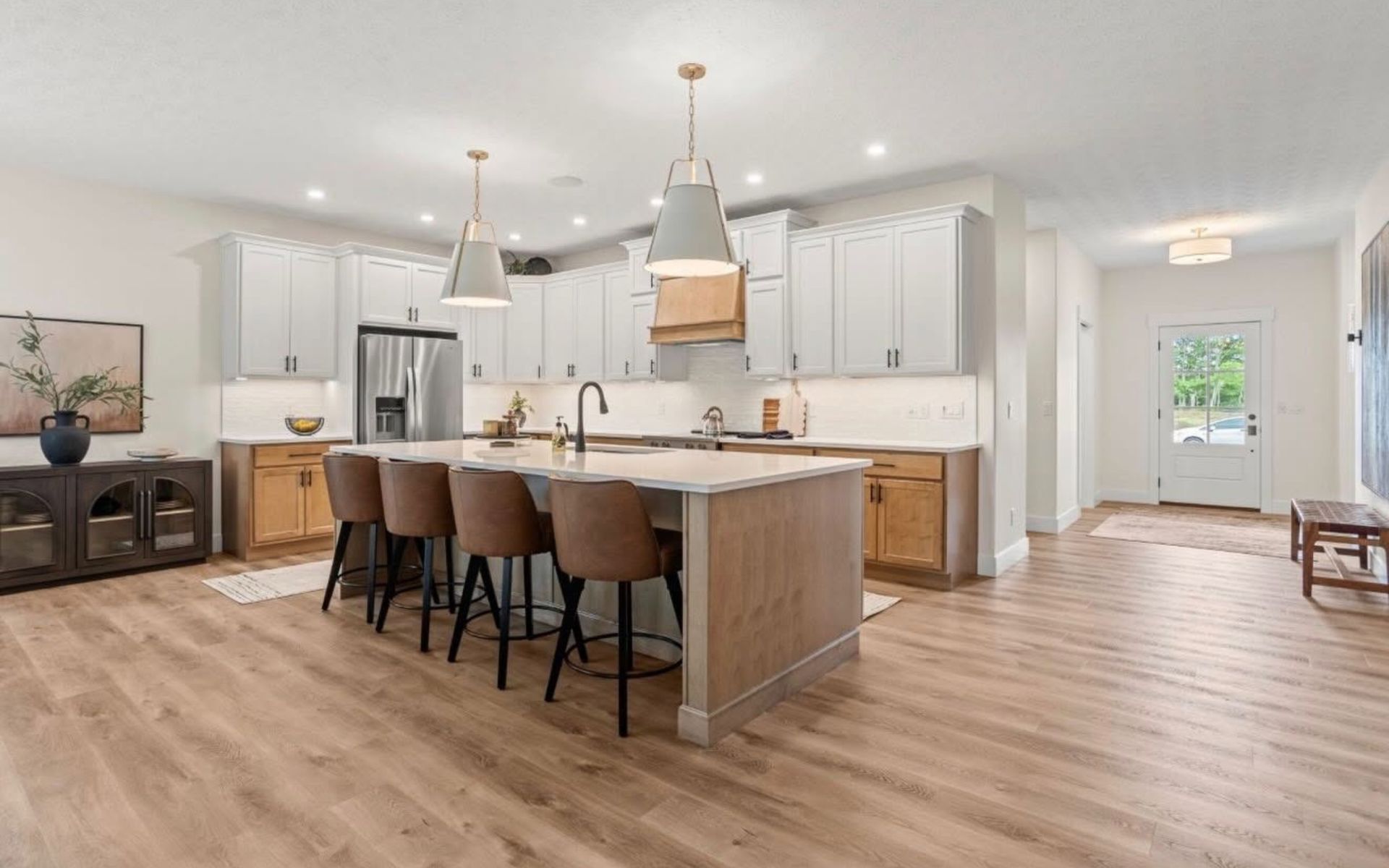 Bright open kitchen with white cabinets, wood island, pendant lights, and bar stools.