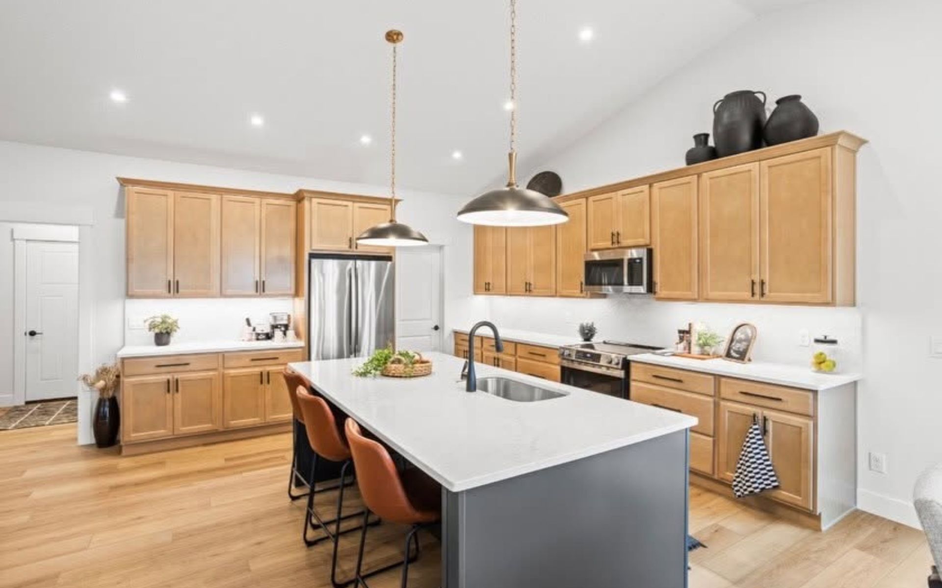 Bright modern kitchen with white island, wood cabinets, pendant lights, and stainless steel appliances