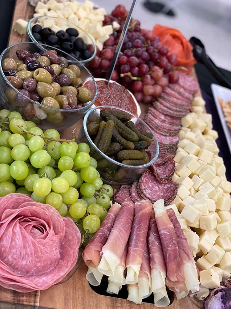 a cutting board filled with meat , cheese , grapes , olives and pickles
