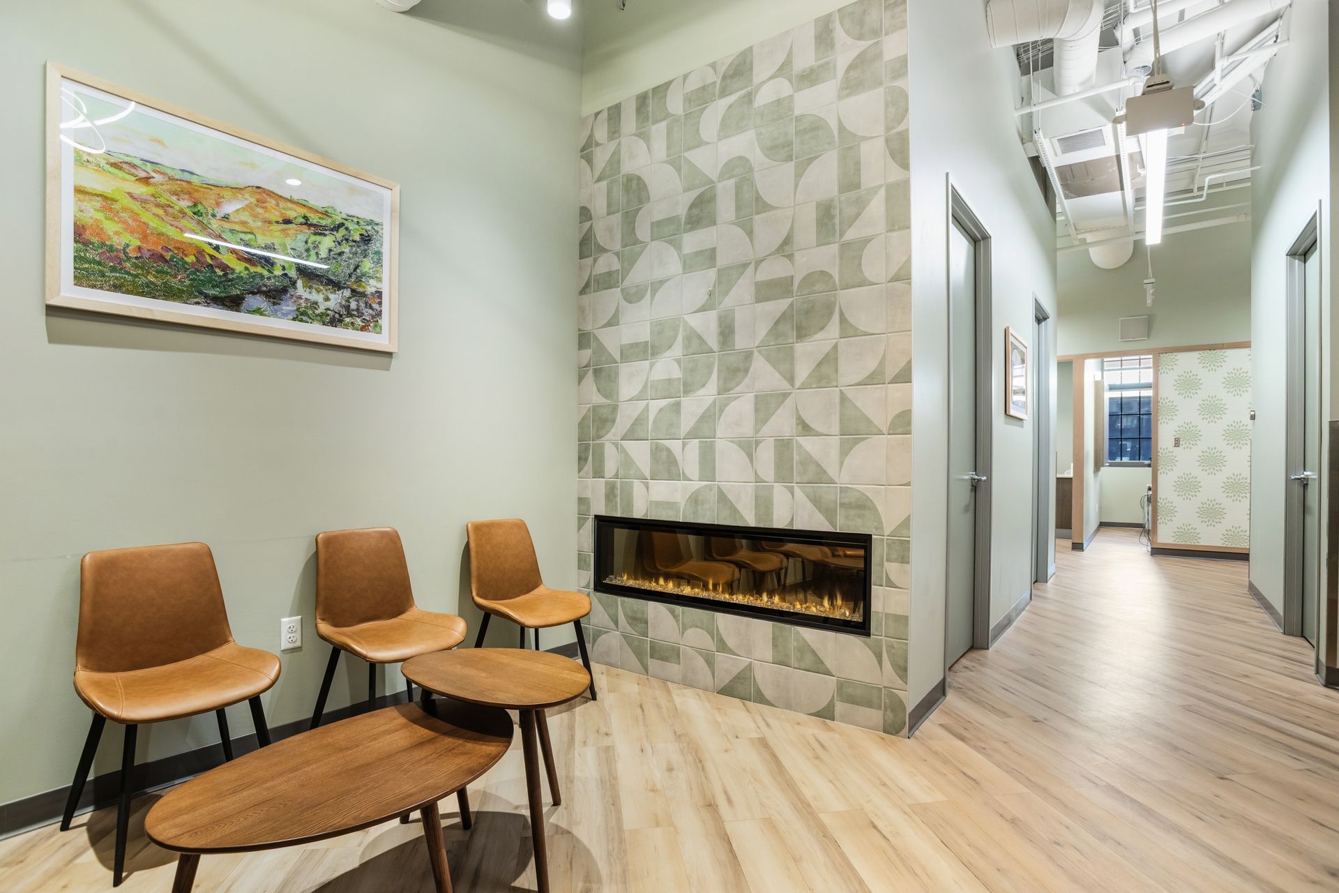 Waiting room with chairs, a fireplace, artwork, and a hallway with doors.