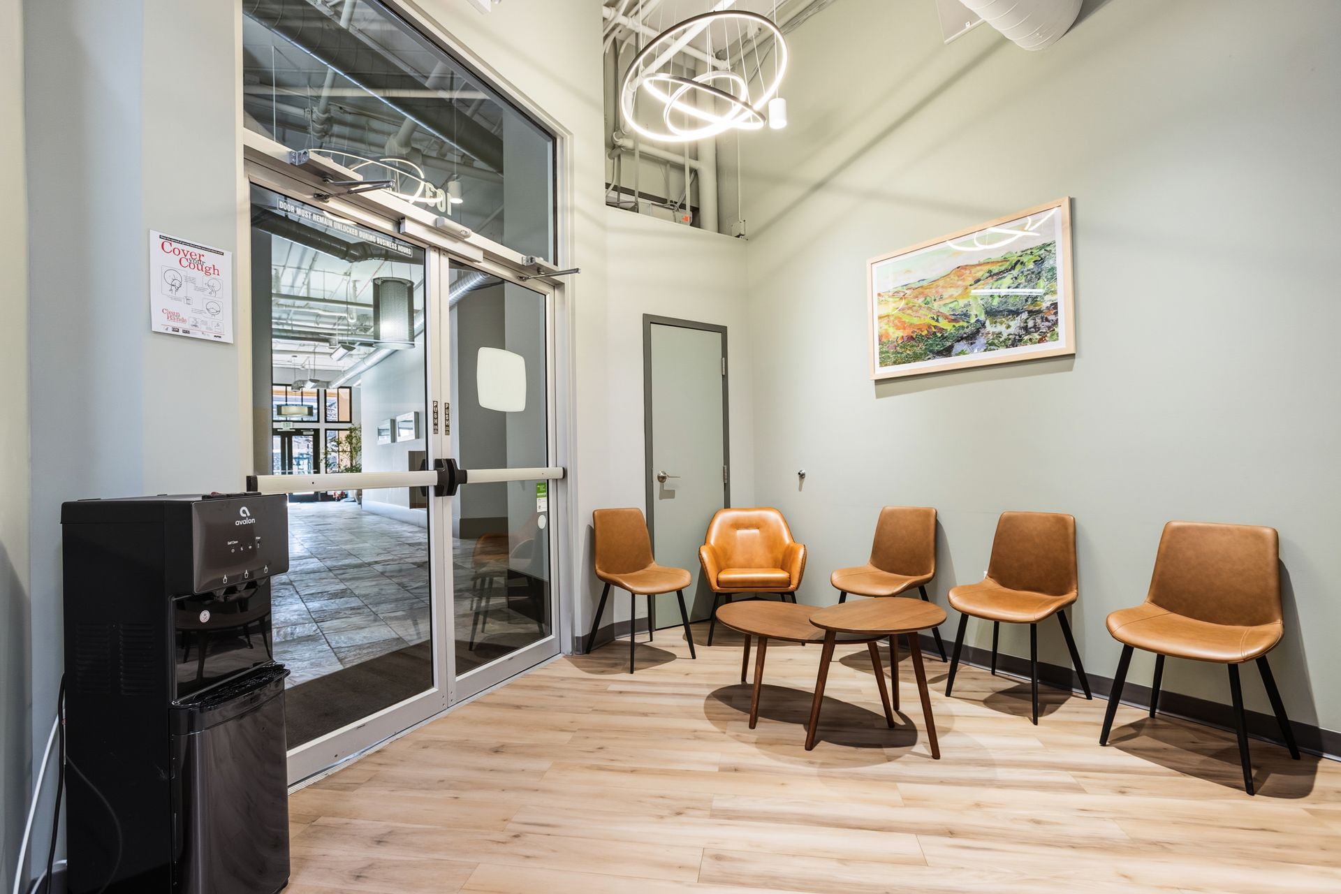 Reception area with seating, artwork, water dispenser, and glass door leading to an interior space.