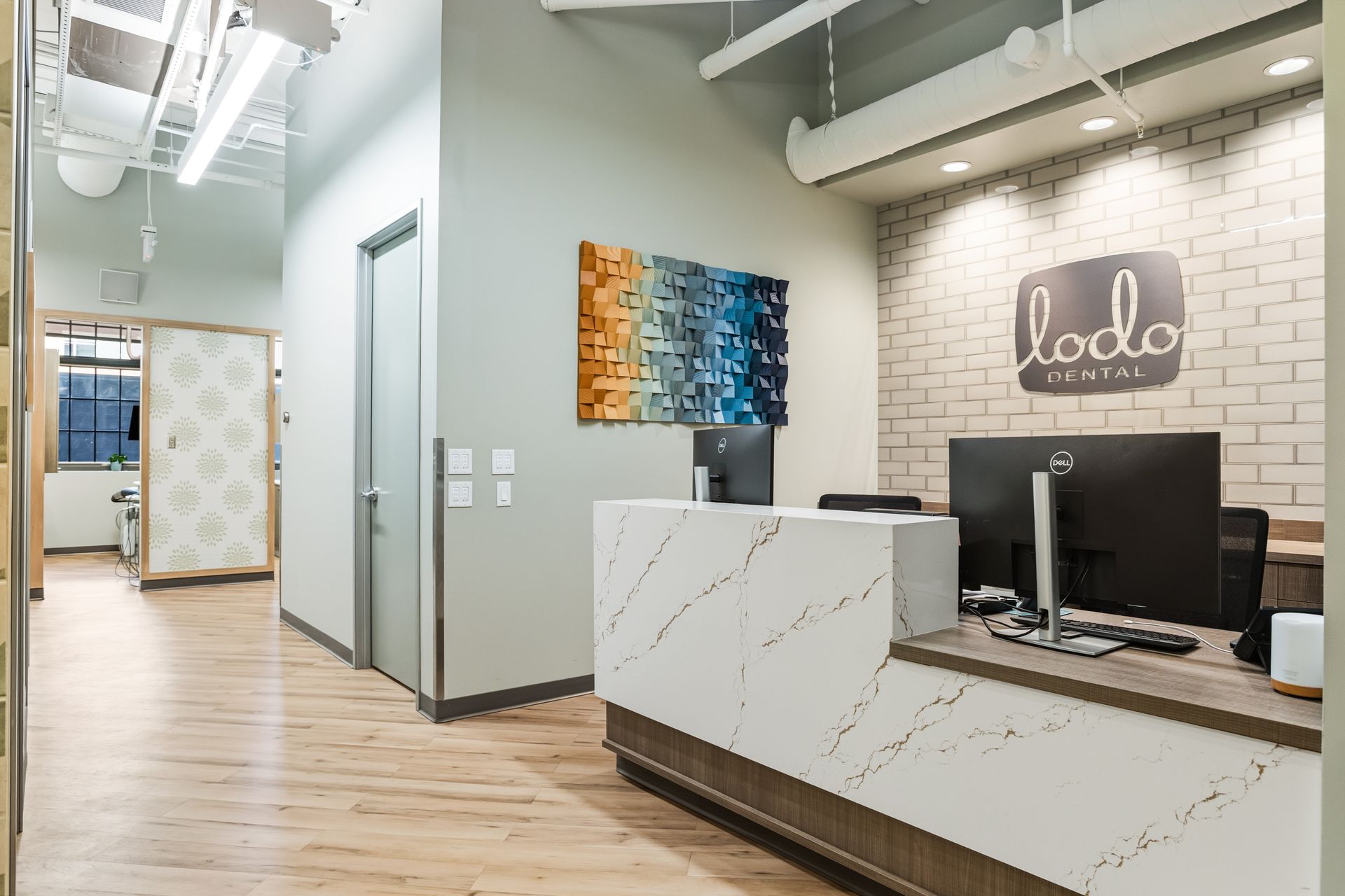Reception area with white brick a reception desk wood flooz and art. The logo 