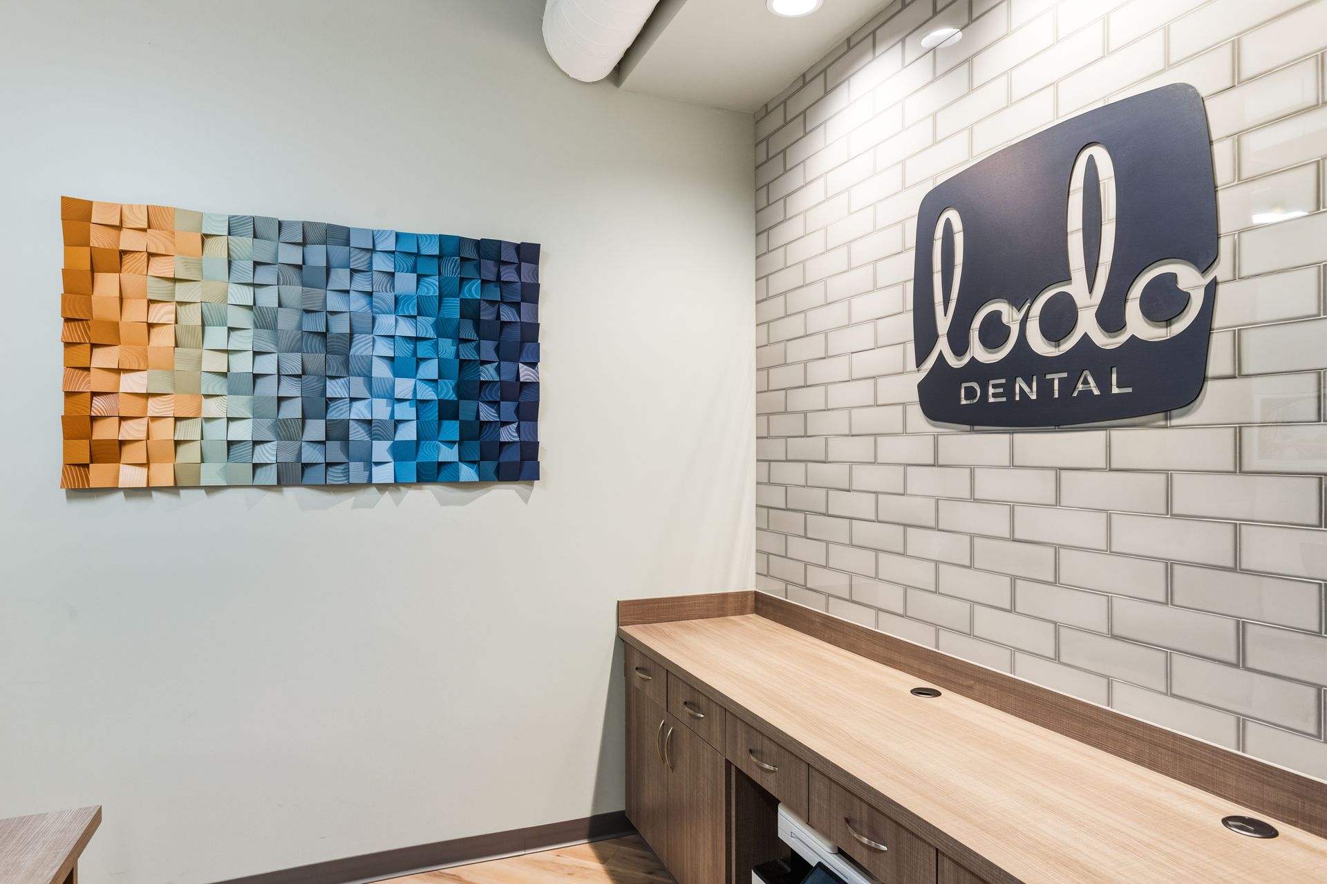 Lodo Dental office waiting area with wooden art piece and logo on brick wall. Wooden countertop with cabinets.