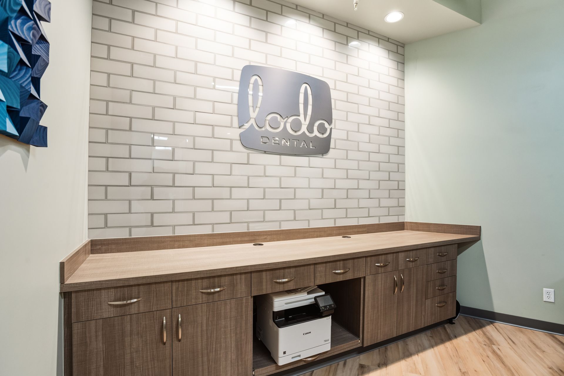 Office area with a countertop and cabinets printer and a lodo dental logo on a brick wall.