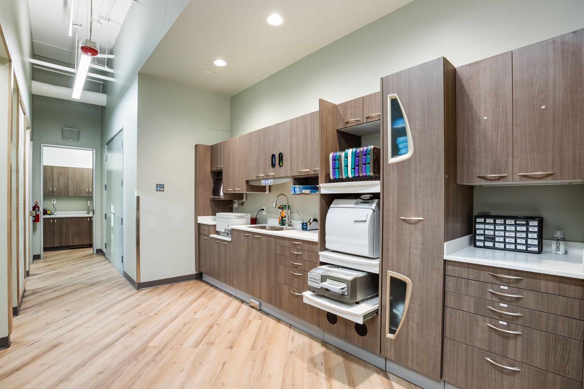 Dental office hallway with light wood cabinetry, sterilizers, and a sink.