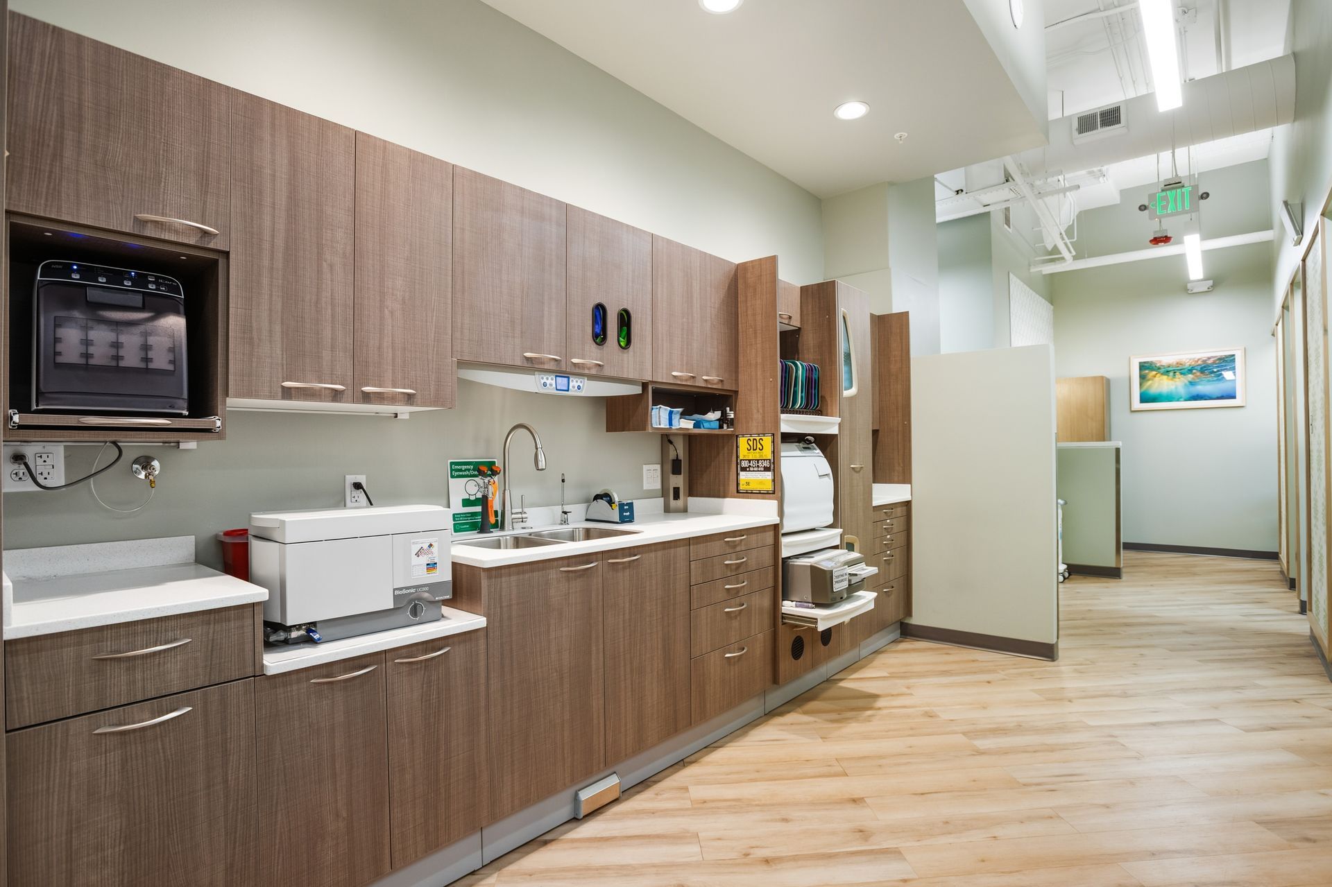 Dental office sterilization room with wooden cabinets, stainless steel equipment, and hallway.