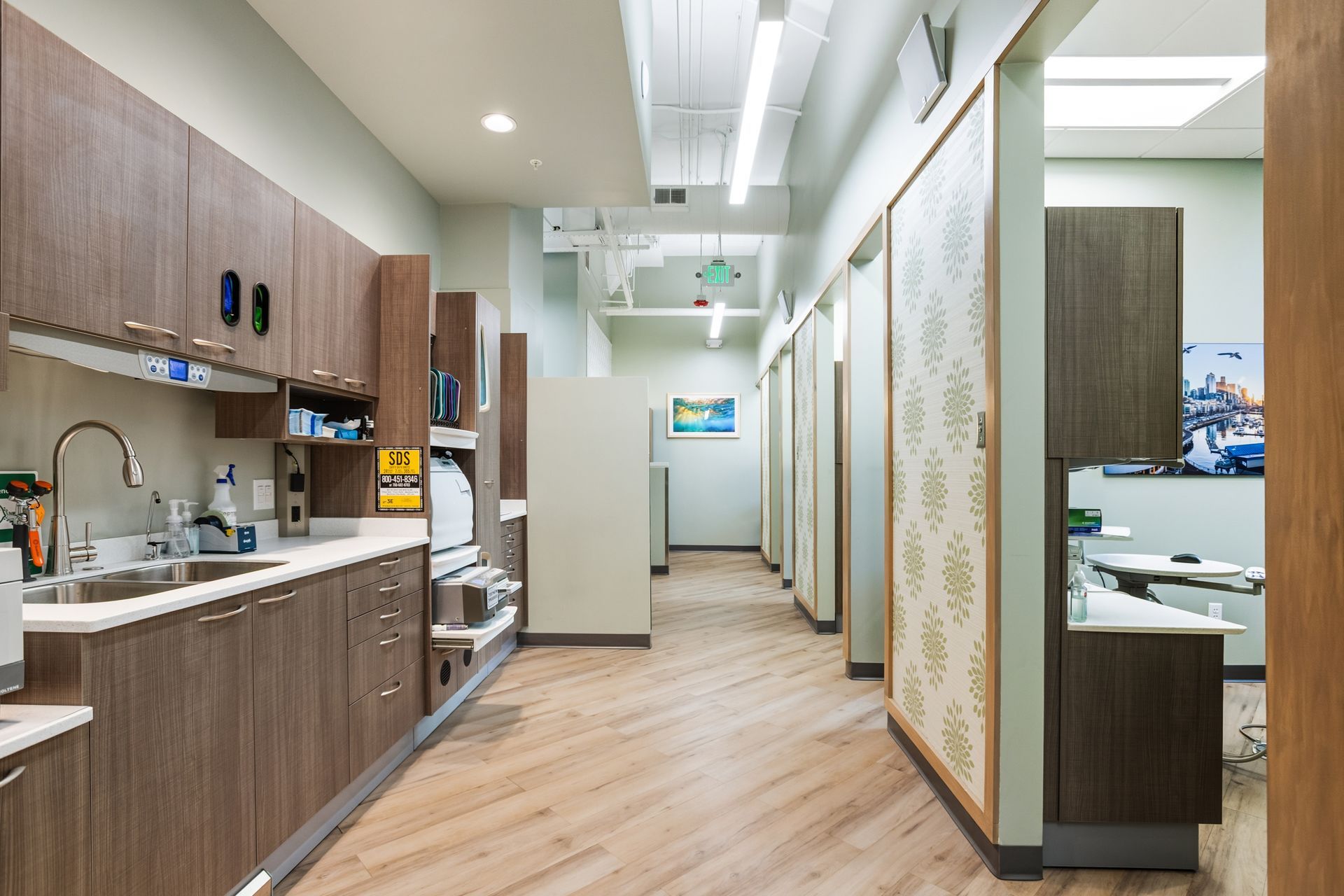 Dental office hallway with light wood cabinetry and flooring, treatment rooms, and decorative sliding doors.