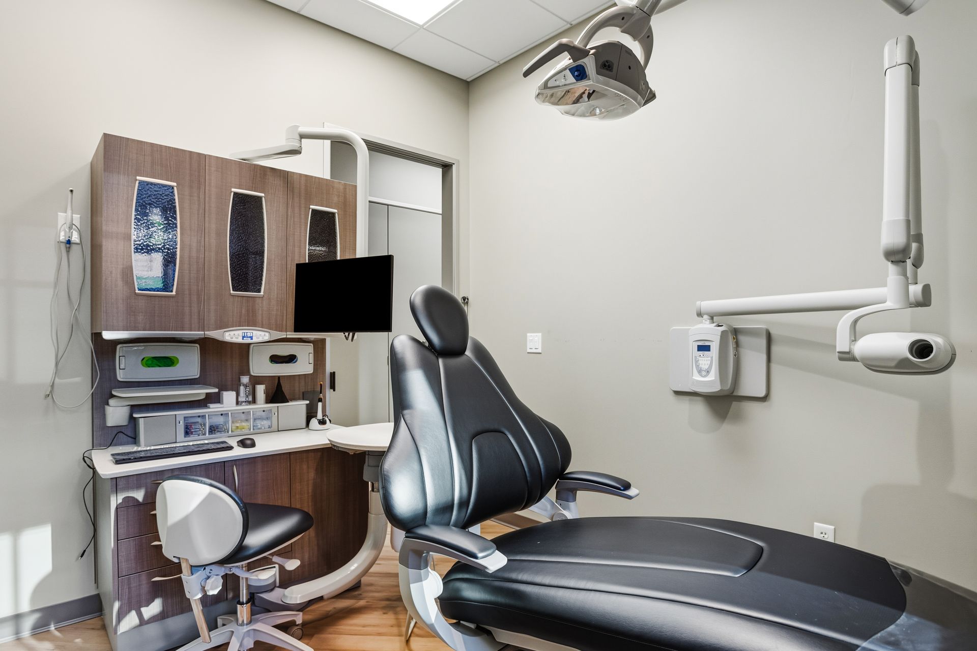 Dental office exam room, dental chair, equipment, and cabinets, gray walls, empty.