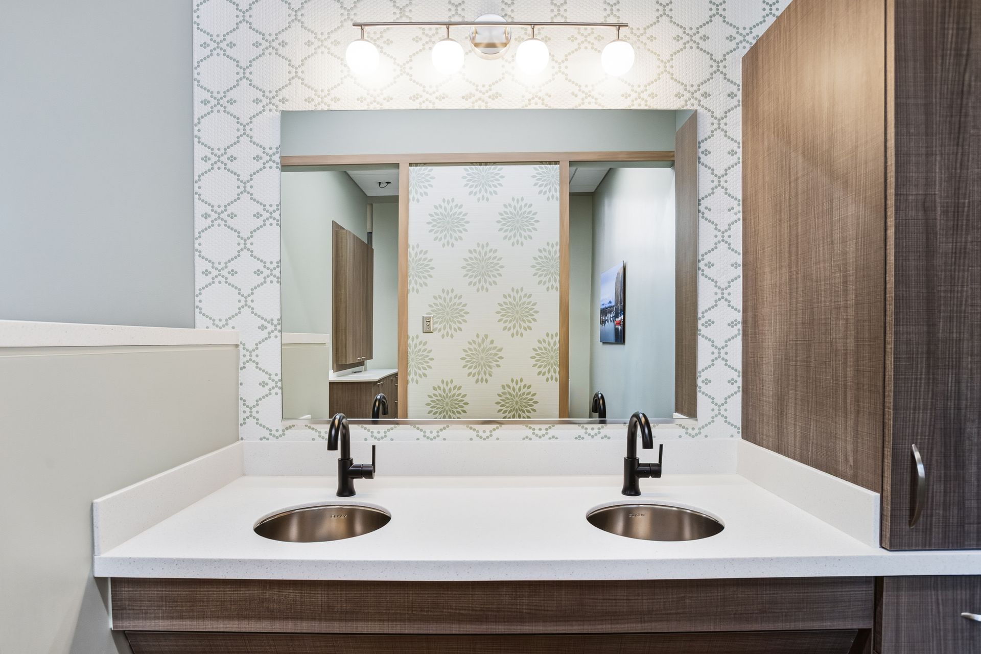 Bathroom with double sinks, large mirror, patterned backsplash, and wooden cabinets.