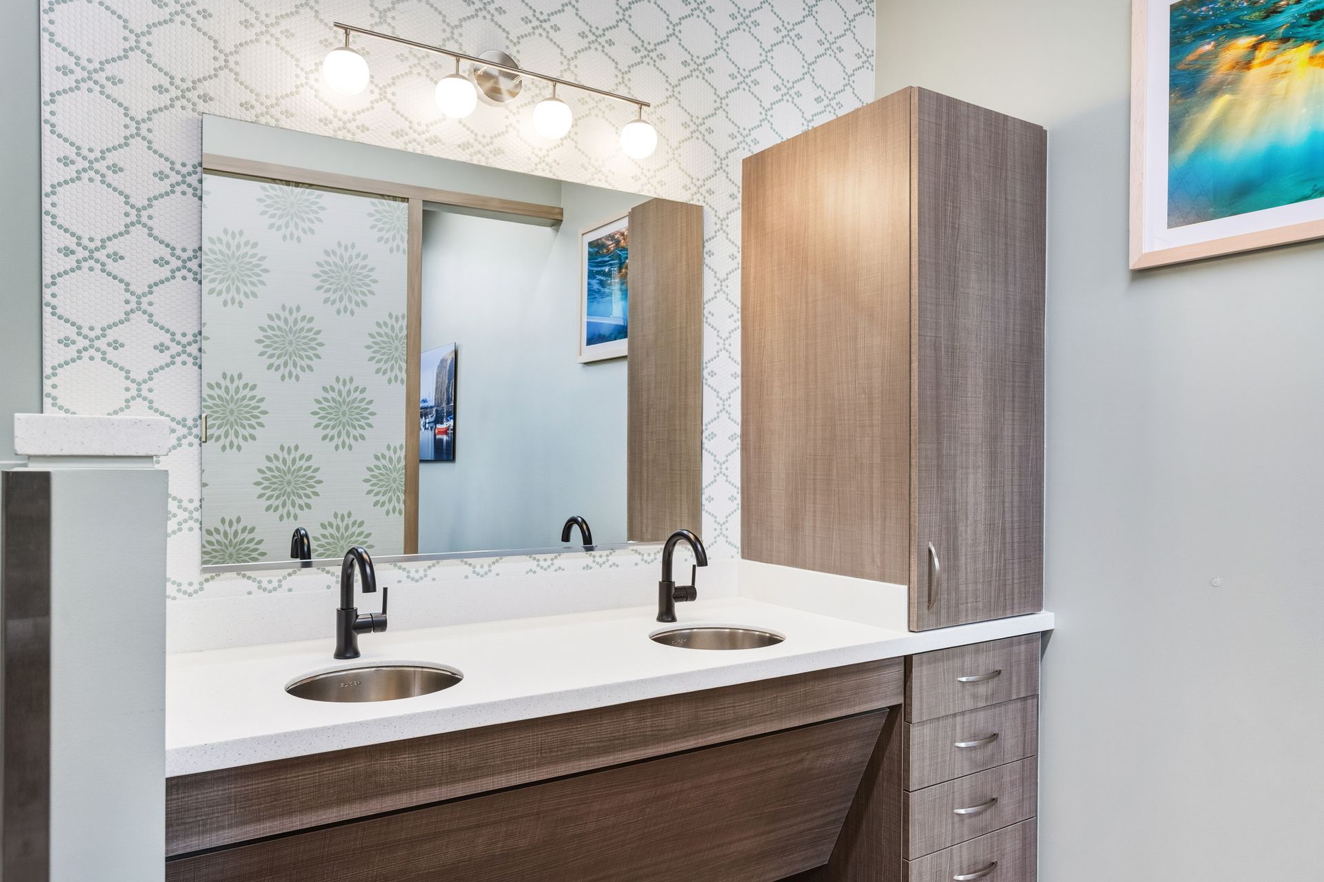 Bathroom with dual sinks, overhead lighting, patterned backsplash, and gray cabinets.